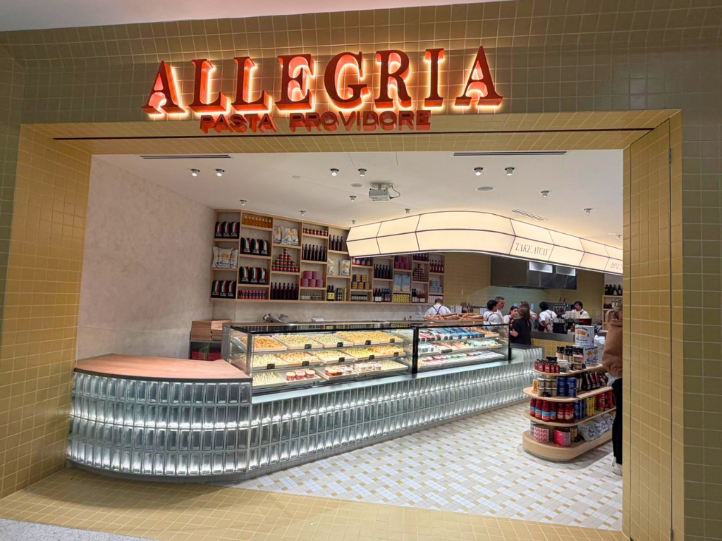 The entrance to the Allegria Pasta Providore restaurant, featuring a large illuminated red and orange sign above a modern glass display case and curved counter inside a tiled dining area.